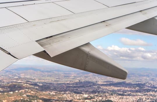 View from passenger window of commercial airplane, blurred urban landscape visible under aircraft wing.