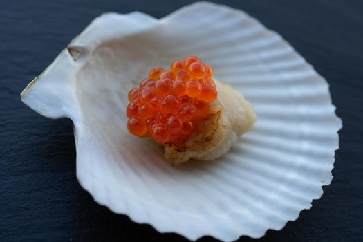Scallop on a shell with a cap of red caviar. Seafood delicacy.