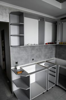 Custom kitchen cabinets installation without a furniture facades mdf. Gray modular kitchen from chipboard material on a various stages of installation in kitchen with a grey tile on floor and walls