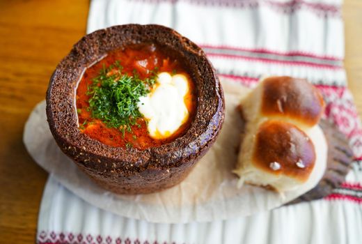 Borscht in black bread with dumplings on an embroidered tablecloth.