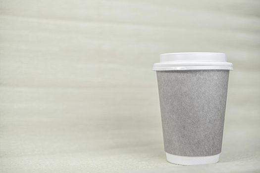 Paper cup of coffee closed with a white lid on a yellow background. There is a place for the text.