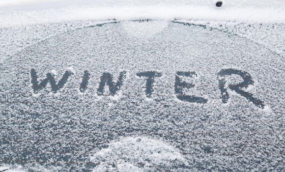 word winter handwritten on snowy car window at winter morning light.