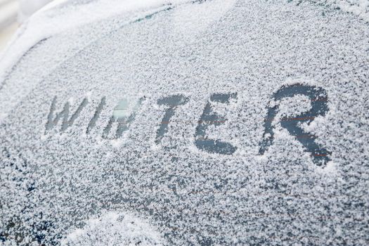 word winter handwritten on snowy car window at winter morning light.