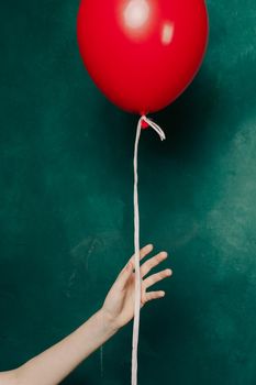 inflatable red balloon in a female hand on a green background close-up. High quality photo