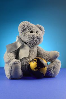 A soft teddy bear hugs the globe of the Earth closely.