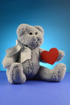 A blue soft teddy bear giving a red heart of a loving embrace.