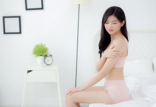 Beautiful young asian woman applying moisturizer with makeup of cosmetic, girl hand touch shoulder cream and lotion attractive, beauty perfect with wellness in the bedroom with skin care concept.