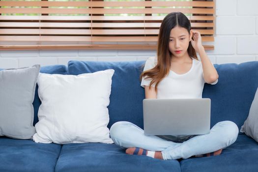 Young asian business woman smile and work from home with laptop computer online to internet on sofa in living room, freelance girl using notebook on couch with comfort, new normal, lifestyle concept.