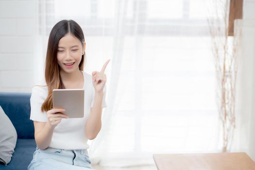 Young attractive asian woman resting using browsing tablet computer on sofa at home, happy girl sitting on couch relax looking digital gadget with excited, communication and lifestyle concept.