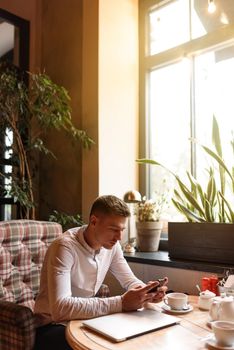 Handsome young man working in cafe while using mobile phone. Lifestyle concept