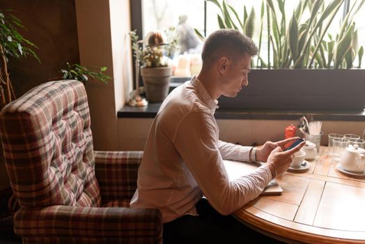 Side view of young businessman holding smartphone while sitting at the table in coffee shop. Lifestyle concept