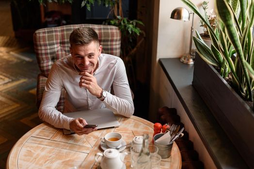 Top view of happy young businessman using smartphone while sitting at the table in cafe. Lifestyle concept