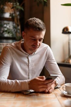 Waist up of handsome young man using mobile phone while looking at screen and typing in cafe. Lifestyle concept