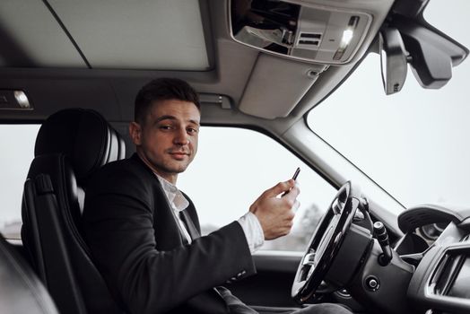 Portrait of smiling young man holding smartphone while driving car. Rent and trade-in concept