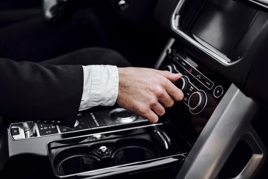 Close up of male hand turning on car air conditioning system. Transportation and vehicle concept