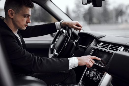 Cropped photo of handsome young man pushing touchpad while driving a car in the city. Rent and trade-in concept
