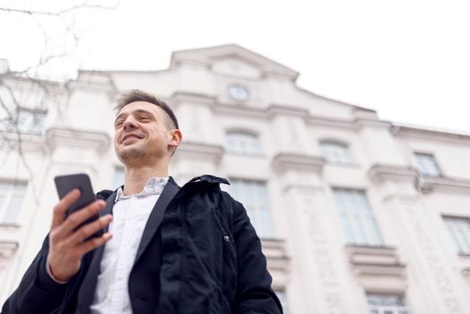 Low angel of happy handsome man using mobile phone while walking on the street. Copy space. Lifestyle concept