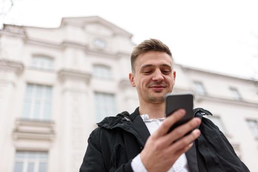 Happy young man sending a message on smartphone outdoors. Copy space. Lifestyle concept