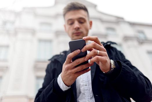 Low angel of handsome guy typing on mobile phone with building on the background. Lifestyle concept