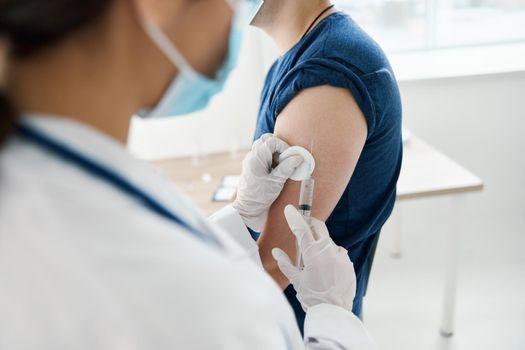 doctor gives an injection in the shoulder Patient in T-shirt Patient in a blue T-shirt in a blue T-shirt. High quality photo