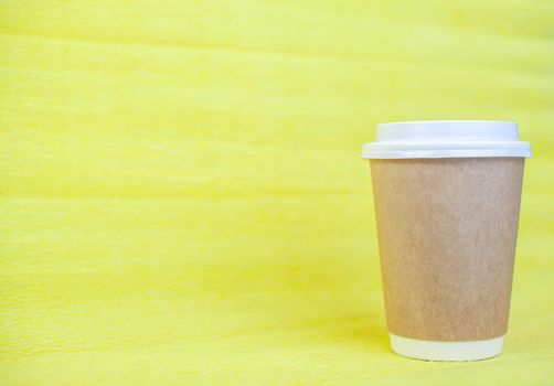 Paper cup of coffee closed with a white lid on a yellow background. There is a place for the text.