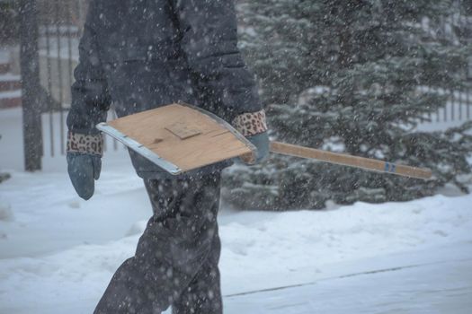 A working man of the municipal service with a snow shovel walks along the road in a storm, blizzard or snowfall in winter in bad weather in the city.Extreme winter weather conditions in the north.