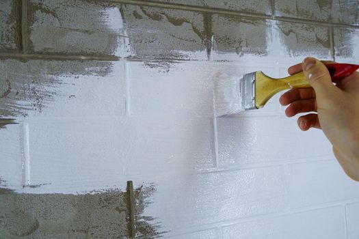 A construction worker applies paint to a brick wall.The painter paints primers the walls with a brush, makes repairs in the house or room.Reconstruction of the building, specialist restores the wall                           