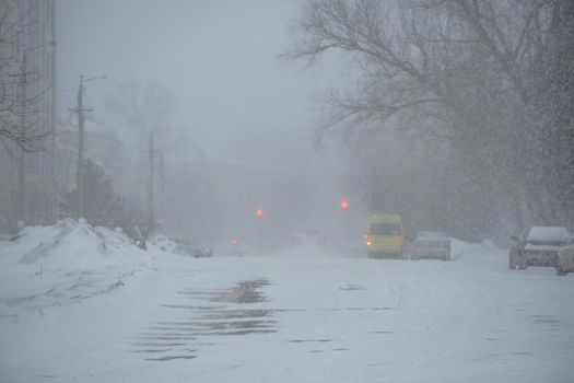 An empty snow-covered road in a storm, blizzard or snowfall in winter in bad weather in the city. Extreme winter weather conditions in the north.