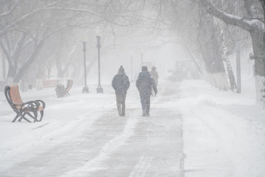 A snow-covered road with people in a storm,blizzard or snowfall in winter in bad weather in the city.Extreme winter weather conditions in the north.People walk through the streets under heavy snowfall