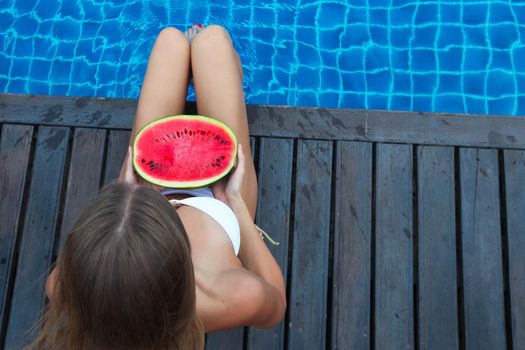 Beautiful woman with fit, tanned body in bikini with watermelon tanning poolside