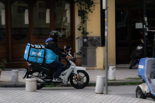 Day view of male with helmet riding motorcycle to deliver take away order contained on a company logo box.