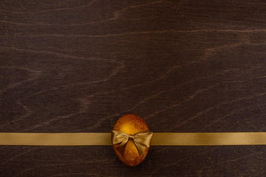 Golden luxury easter egg and ribbon composition on dark wooden background with copy space for text card