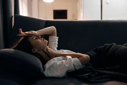 a woman lies on the sofa covered with a blanket feeling unwell hand on head. High quality photo