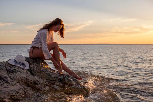 Beautiful woman enjoying sunset on the beach, sitting on rocks