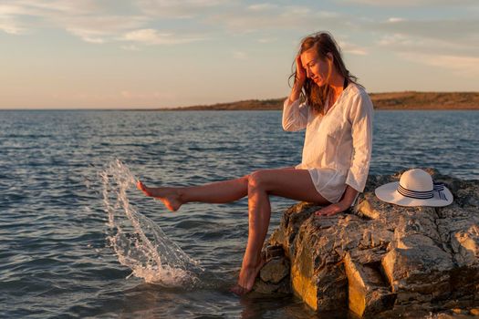 Beautiful woman enjoying sunset on the beach, sitting on rocks