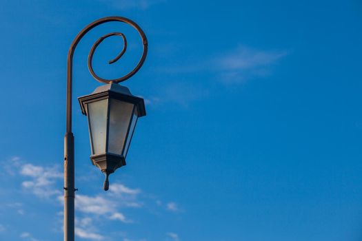 Low-angle view of antique style lampposts against a bright blue sky.