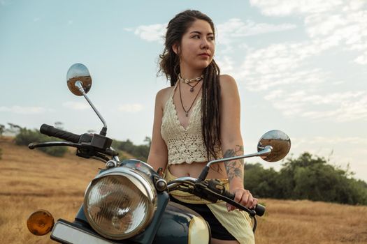 A woman sits on a motorcycle in a field waiting for sunset