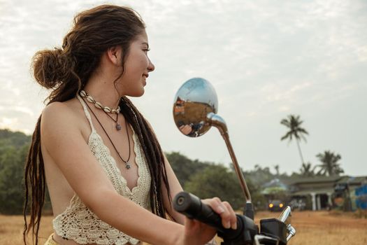 A woman sits on a motorcycle in a field waiting for sunset, back view