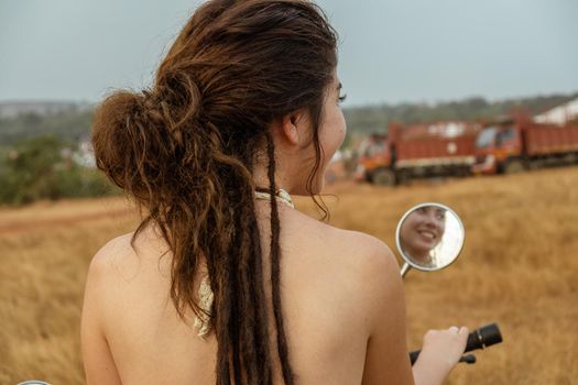 A woman sits on a motorcycle in a field waiting for sunset, back view