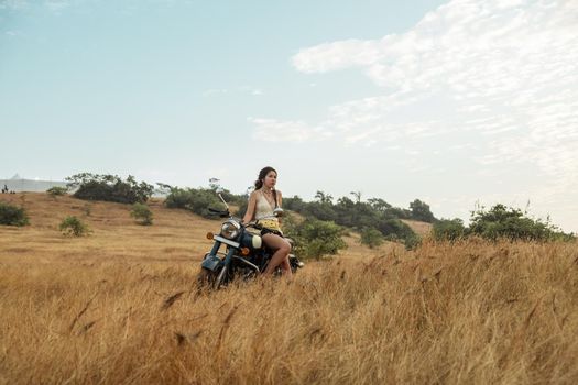 A woman sits on a motorcycle in a field waiting for sunset