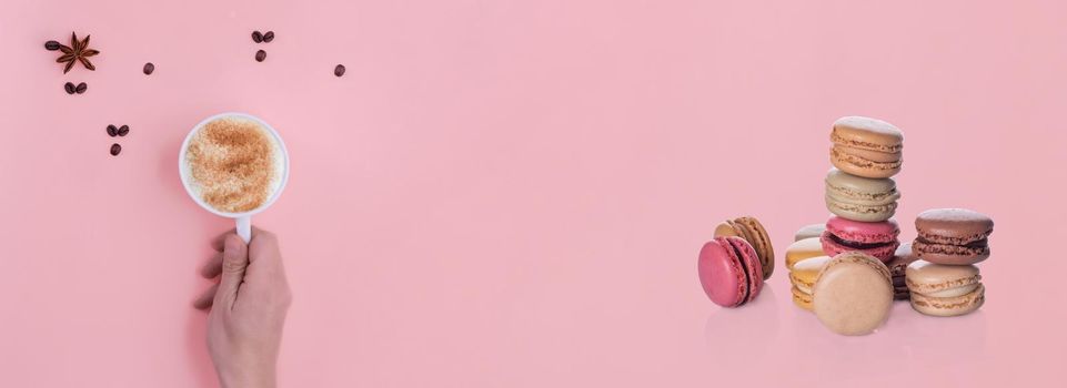 banner of hand holding a cup of coffee and macaroons on pink background