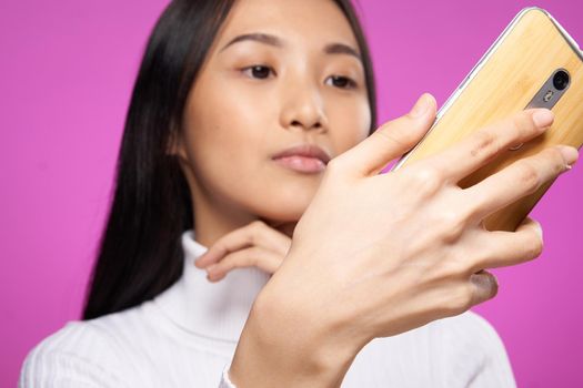 woman asian appearance phone in hands close-up technology gadget pink background. High quality photo