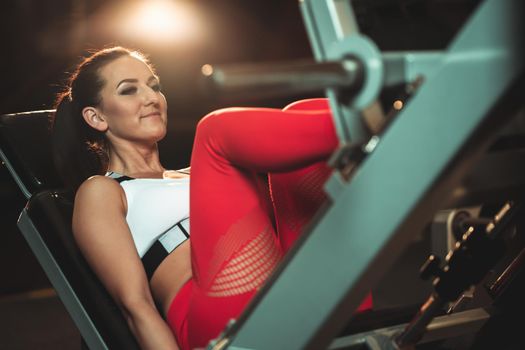 Young woman practicing legs on the machine in a gym.