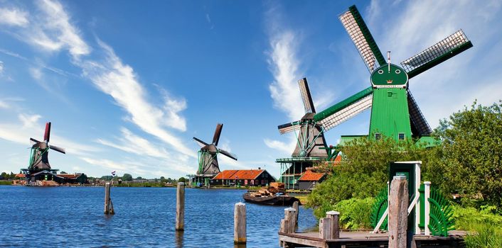 ZAANSE SCHANS, NETHERLANDS - CIRCA AUGUST 2020: Dutch windmill in green countryside close to Amsterdam, with blue sky and river water.