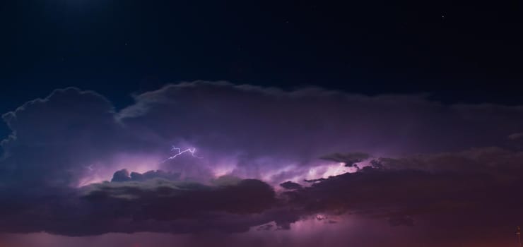Lightnings in heavy, purple storm clouds at night.
