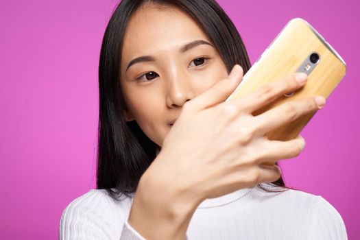 pretty brunette with a phone in her hands chatting internet online pink background. High quality photo