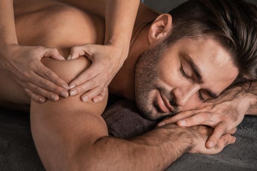 A good-looking man getting a back massage lying down at spa, Woman hand making sign heart love concept