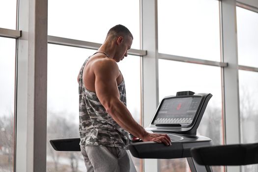 Muscular athletic bodybuilder fitness model running treadmill gym near big window jogging stationary machine do cardio training Weight loss Healthy lifestyle concept. Back view rear