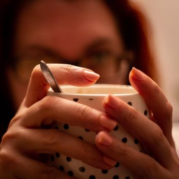 Close-up of a woman holding a white cup with black dots containing a hot drink