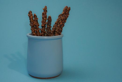 Chocolate crispy sticks with hazelnut sprinkles on a blue background.